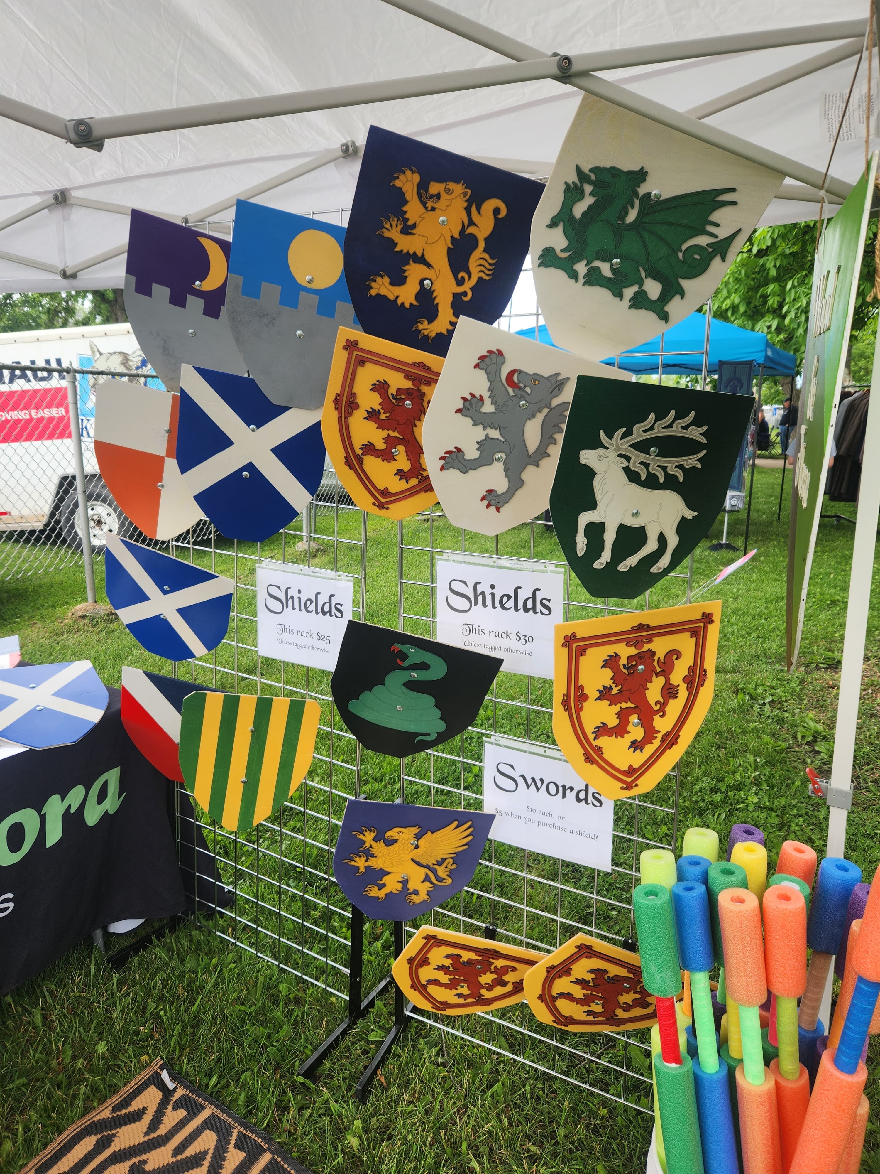 Our handmade shields displayed at an outdoor event, next to our live-event exclusive foam swords. En garde!
Check out our shop to customize your own heater or round shield, or browse our special collections!